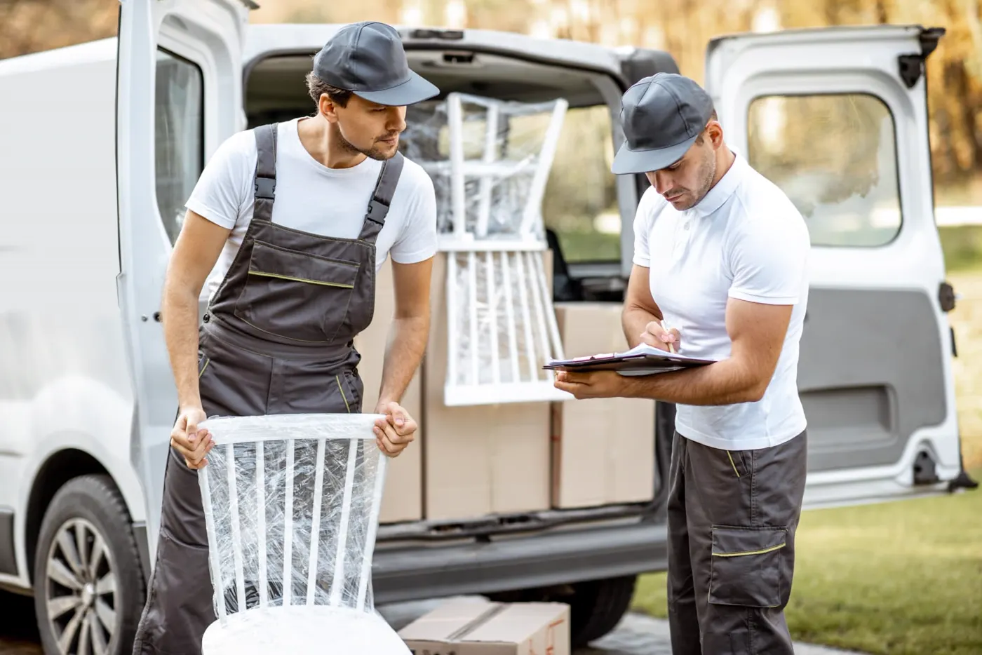 Two movers with a wrapped chair and paperwork at a van