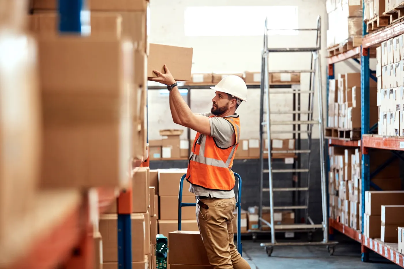 Worker in a hard hat reaching for boxes on warehouse shelving